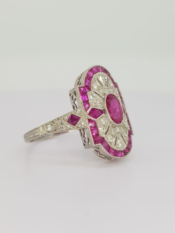 Art Deco Style Ruby Diamond and Platinum Plaque Ring; central oval faceted ruby surrounded by diamonds and outer calibre-cut ruby border, ruby and diamond set shoulders