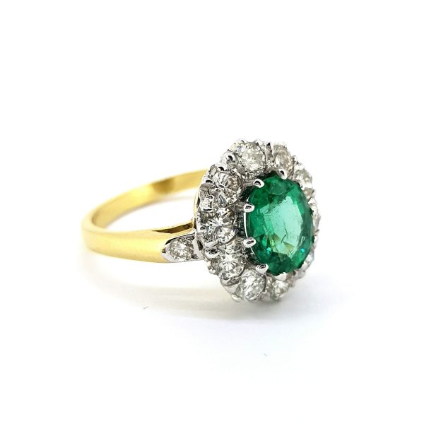 Vintage Emerald and Diamond Cluster Ring; central 1.00ct oval emerald surrounded by 1.25cts brilliant-cut diamonds, diamond-set shoulders, in 18ct white gold to a plain 18ct yellow gold band