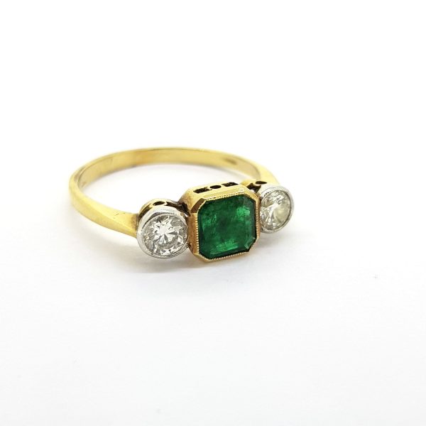 Emerald and Diamond Three Stone Ring; central octagonal step-cut emerald flanked by brilliant cut diamonds, 18ct yellow gold band