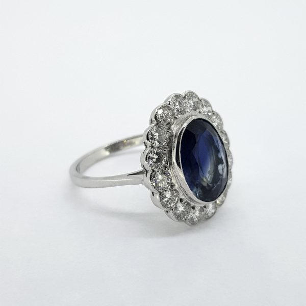 Sapphire and Diamond Oval Floral Cluster Ring; 4.55ct oval sapphire within a 1.25ct round brilliant-cut diamond surround, in 18ct white gold