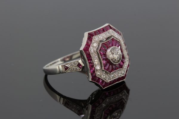 Art Deco Style Ruby and Diamond Cluster Dress Ring in Platinum; central diamond surrounded by alternated borders of calibre cut rubies and diamonds