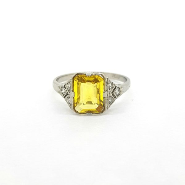 Art Deco Style Emerald Cut Yellow Sapphire and Diamond Cluster Ring; central 2ct emerald-cut yellow sapphire with diamond set shoulders, in 18ct white gold