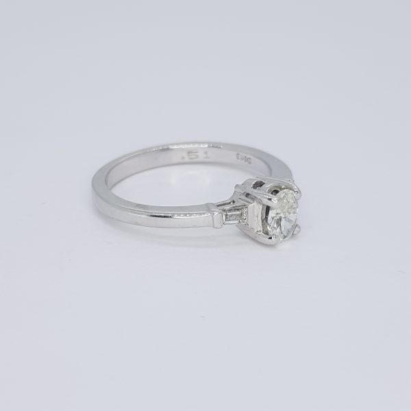 Diamond Solitaire Engagement Ring with Baguette Shoulders in 18ct White Gold; featuring a central claw-set round brilliant-cut diamond flanked by tapered baguette cut diamonds to the shoulders in rubover settings