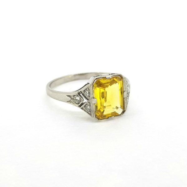 Art Deco Style Emerald Cut Yellow Sapphire and Diamond Cluster Ring; central 2ct emerald-cut yellow sapphire with diamond set shoulders, in 18ct white gold