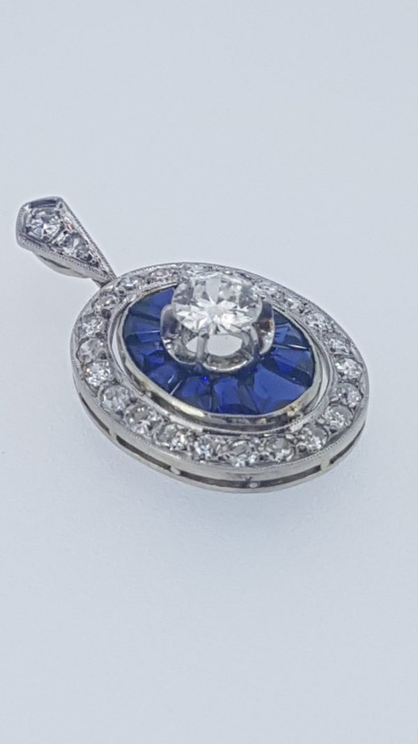 Vintage Calibre Cut Sapphire and Diamond Pendant; central 0.75 carat diamond surrounded by calibre-cut sapphires and outer border of diamonds, diamond set bale, in 18ct white gold, Circa 1960s