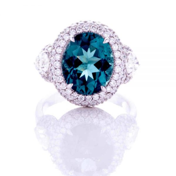 4.69 Oval Indicolite Tourmaline and Diamond Cluster Dress Ring; central 4.69ct oval-cut blue-green indicolite tourmaline surrounded by a double border of brilliant-cut diamonds, with rose-cut and brilliant-cut diamond-set shoulders, in 18ct white gold