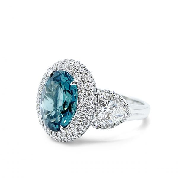 4.69 Oval Indicolite Tourmaline and Diamond Cluster Dress Ring; central 4.69ct oval-cut blue-green indicolite tourmaline surrounded by a double border of brilliant-cut diamonds, with rose-cut and brilliant-cut diamond-set shoulders, in 18ct white gold