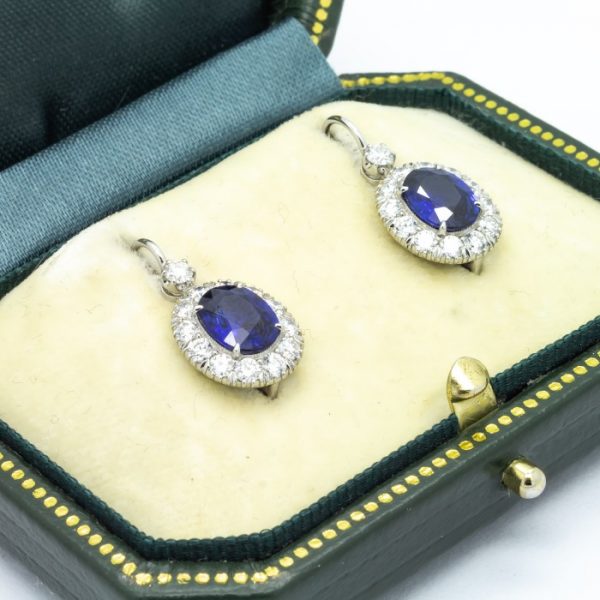 Sapphire, Diamond and Platinum Oval Cluster Drop Earrings; featuring 2.43ct oval faceted sapphires surrounded by round brilliant-cut diamonds, suspended from a single round brilliant cut diamond