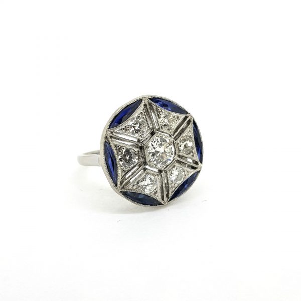 French Calibre Cut Sapphire and Diamond Cluster Dress Ring in Platinum; central round brilliant-cut diamond surrounded by six diamond set sections radiating out to form a star, all surrounded by calibre-cut diamond set edges