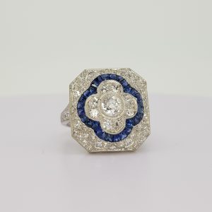 Sapphire and Diamond Cluster Dress Ring; central diamond floral cluster with calibre sapphire border, all within a diamond surround, in 18ct white gold