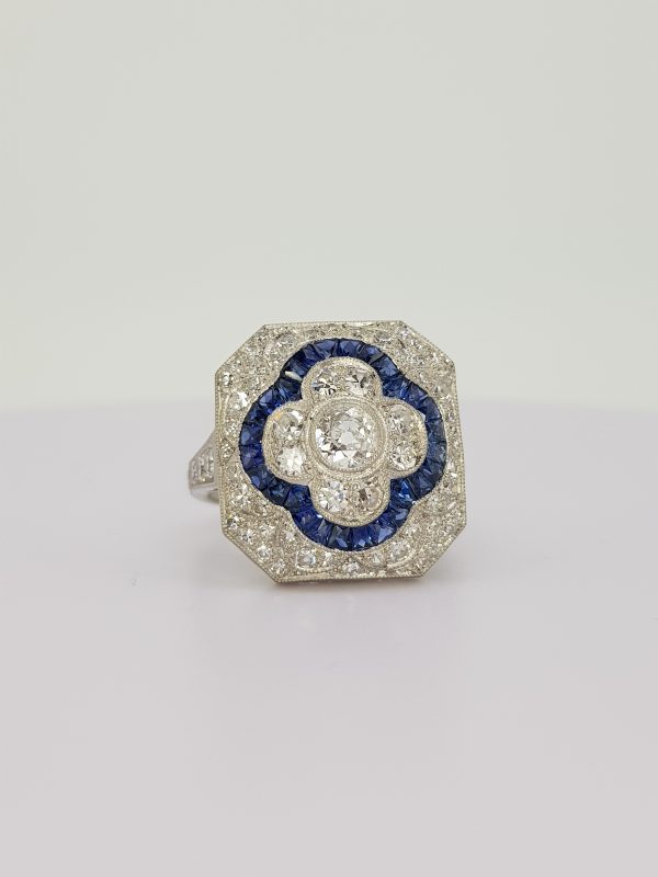 Sapphire and Diamond Cluster Dress Ring; central diamond floral cluster with calibre sapphire border, all within a diamond surround, in 18ct white gold