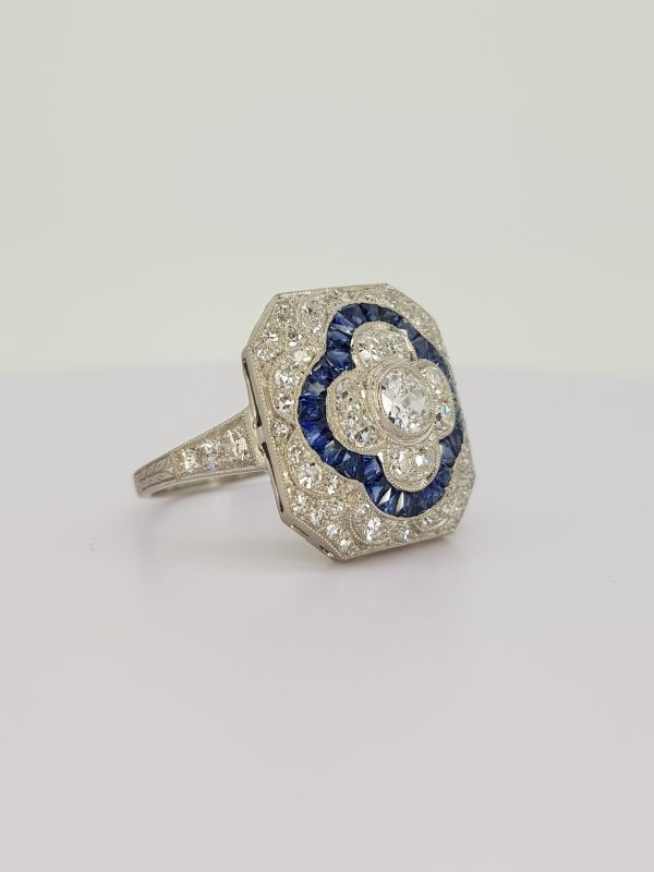 Sapphire and Diamond Cluster Dress Ring; central diamond floral cluster with calibre sapphire border, all within a diamond surround, in 18ct white gold
