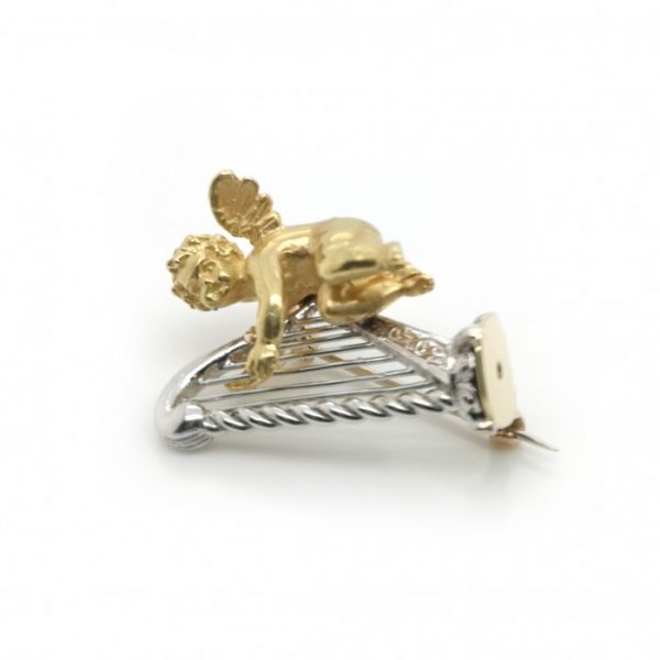 Gold Cherub and Harp Brooch; designed as an 18ct yellow gold cherub, in flight, playing an 18ct white gold harp