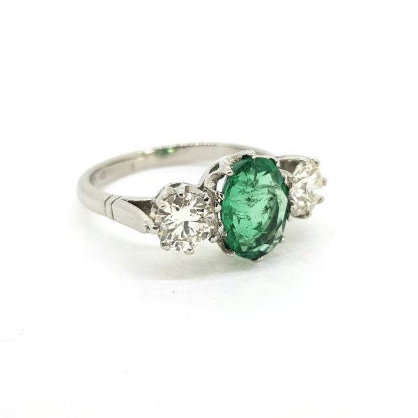 Emerald and Diamond Three Stone Ring in Platinum; central 1.80ct oval emerald flanked by 1.05cts brilliant-cut diamonds