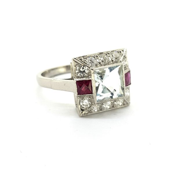 Aquamarine, Ruby and Diamond Cluster Ring in Platinum; central 1.30ct square shaped aquamarine surrounded by 0.60cts diamonds with French cut rubies to the sides
