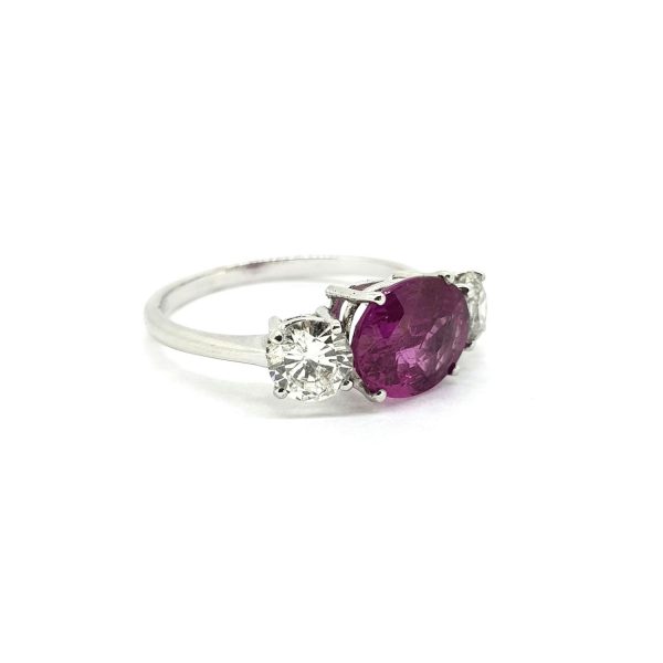 Pink Sapphire and Diamond Three Stone Ring; central 2.30ct oval pink sapphire flanked by 0.97cts brilliant-cut diamonds, claw set and mounted in 18ct white gold