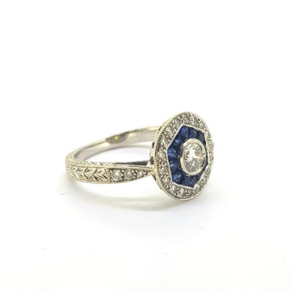 Vintage Sapphire and Diamond Cluster Target Ring, central brilliant-cut diamond surrounded by a hexagon of French cut sapphires and outer border of 18 brilliant cut pave set diamonds, in 18ct white gold with decorative engraving, Circa 1960