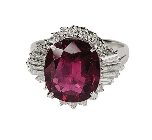 Vintage French 5ct Rubellite and Baguette Diamond Cluster Dress Ring; central 5ct oval vibrant red tourmaline surrounded by brilliant-cut diamonds accented with tapering baguette-cut diamond shoulders, in platinum, Circa 1960