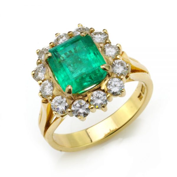3.80ct Emerald Cut Emerald and Diamond Cluster Ring; central 3.8ct emerald-cut emerald within a surround of 12 brilliant-cut diamonds totalling 0.96 carats, in 18ct yellow gold with eye-catching triple-split shoulders
