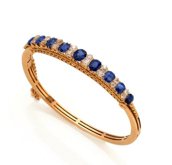 Antique Victorian 7.2ct Natural Sapphire and Diamond Bangle Bracelet; 7.20cts graduated oval natural sapphires with no heat treatment interspaced with two old mine-cut diamonds in solid 18ct yellow gold with fine detailed fret pierced under-gallery work. Late 19th century Circa 1890