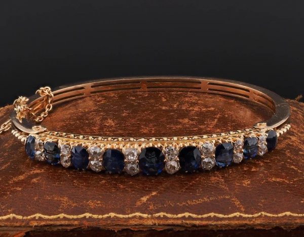Antique Victorian 7.2ct Natural Sapphire and Diamond Bangle Bracelet; 7.20cts graduated oval natural sapphires with no heat treatment interspaced with two old mine-cut diamonds in solid 18ct yellow gold with fine detailed fret pierced under-gallery work. Late 19th century Circa 1890