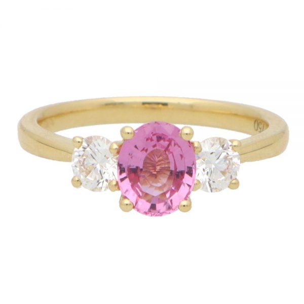 Pink Sapphire and Diamond Trilogy Engagement Ring; central 1.08ct oval cut vibrant pink sapphire flanked by 0.50cts GIA certified diamonds in 18ct yellow gold