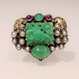 Late Art Deco Jade Clip Brooch by Dorrie Nossiter; carved jade plaque with gold vineleaf shoulders accented with pearls and pink tourmaline, Circa 1930
