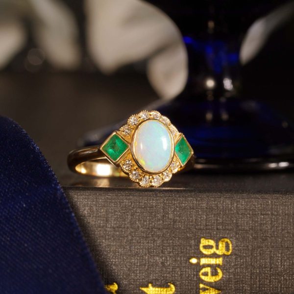 Australian Opal Emerald and Diamond Cluster Dress Ring, central oval cabochon Australian opal accented top and bottom by round brilliant-cut diamonds and square-cut emeralds to the shoulders in 14ct yellow gold