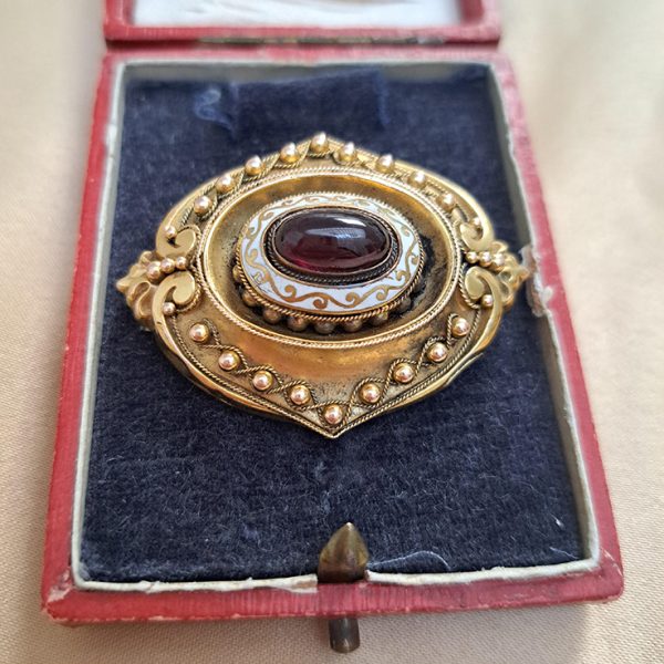 Antique Cabochon Garnet and Gold Locket Brooch, decorative 18ct yellow gold brooch with ball and ropework detailing with central oval cabochon garnet surrounded by white enamel. With locket compartment to reverse