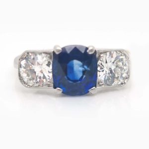 Late Art Deco Sapphire and Diamond Three Stone Engagement Ring, 1.96ct cushion-cut sapphire flanked by 1.20cts old European-cut diamonds in platinum