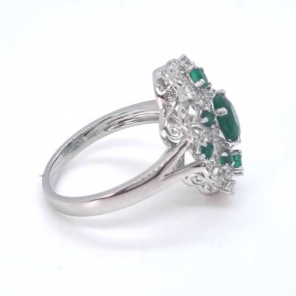 Decorative 1.13ct Emerald and Diamond Cluster Dress Ring, 1.13 carat emerald nestled within entwinned loop diamond surround with emerald accents in 18ct white gold