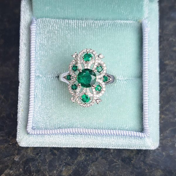 Decorative 1.13ct Emerald and Diamond Cluster Dress Ring, 1.13 carat emerald nestled within entwinned loop diamond surround with emerald accents in 18ct white gold