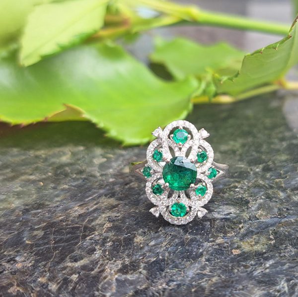 Decorative 1.13ct Emerald and Diamond Cluster Dress Ring, 1.13 carat emerald nestled within entwinned loop diamond surround with emerald accents in 18ct white gold