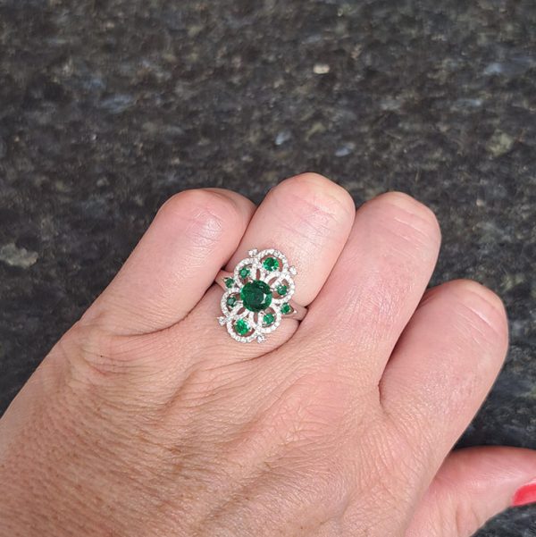 Decorative 1.13ct Emerald and Diamond Cluster Dress Ring, 1.13 carat emerald nestled within entwinned loop diamond surround with emerald accents in 18ct white gold