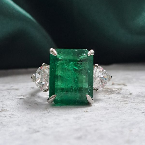 9ct Zambian Emerald and Heart Diamond Three Stone Ring with GIA Certificates, 9.08ct emerald-cut Zambian emerald flanked by GIA certified heart shaped diamonds in platinum