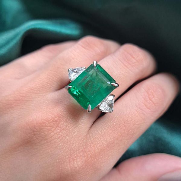 9ct Zambian Emerald and Heart Diamond Three Stone Ring with GIA Certificates, 9.08ct emerald-cut Zambian emerald flanked by GIA certified heart shaped diamonds in platinum