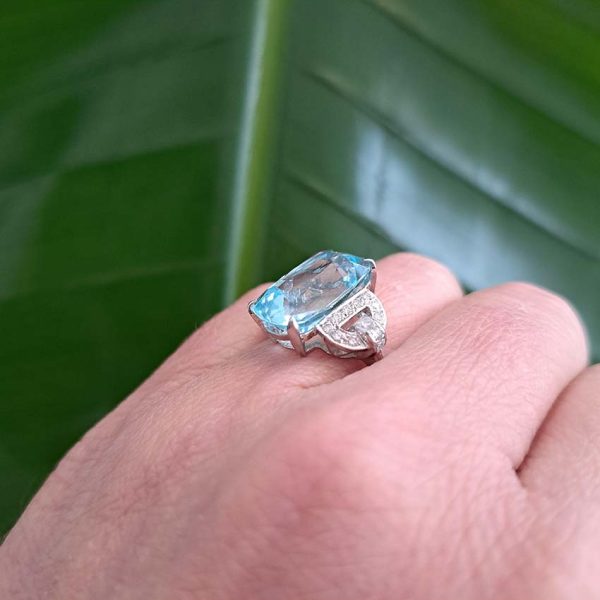 9.43ct Aquamarine and Diamond Dress Ring, large elongated cushion-cut aquamarine flanked by geometric buckle-design diamond-set shoulders in platinum