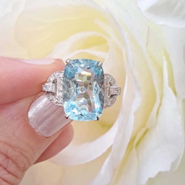 9.43ct Aquamarine and Diamond Dress Ring, large elongated cushion-cut aquamarine flanked by geometric buckle-design diamond-set shoulders in platinum