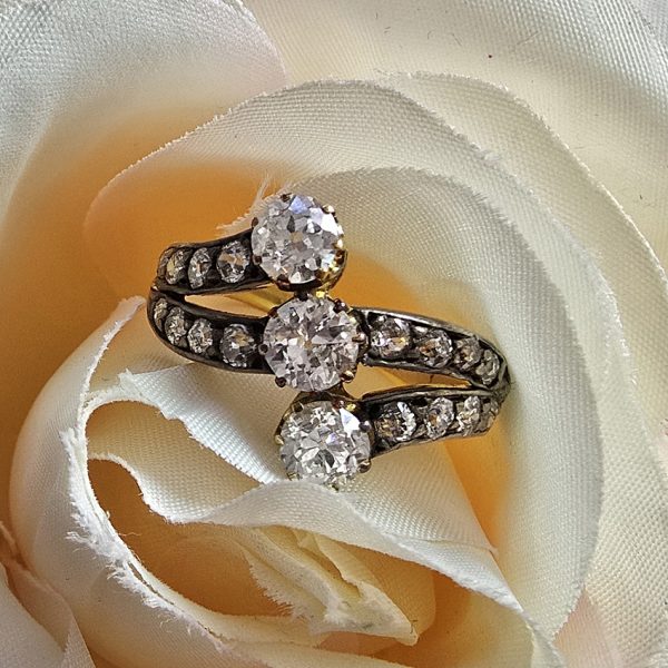 Victorian Antique Diamond Three Stone Banded Ring, diamond trilogy vertically set in asymmetrical design flanked by diamond banded shoulders in silver upon 18ct yellow gold