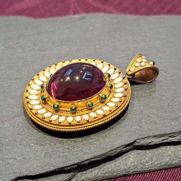 Antique Archaeological Revival Garnet Enamel and Gold Pendant, yellow gold pendant with large oval cabochon-cut garnet accented with white enamel and green enamel decorated surround