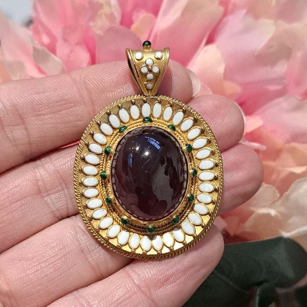 Antique Archaeological Revival Garnet Enamel and Gold Pendant, yellow gold pendant with large oval cabochon-cut garnet accented with white enamel and green enamel decorated surround