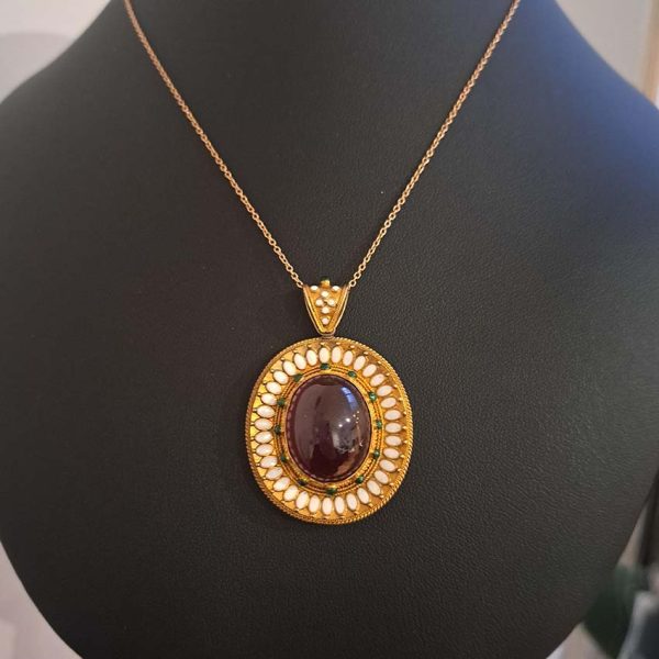 Antique Archaeological Revival Garnet Enamel and Gold Pendant, yellow gold pendant with large oval cabochon-cut garnet accented with white enamel and green enamel decorated surround
