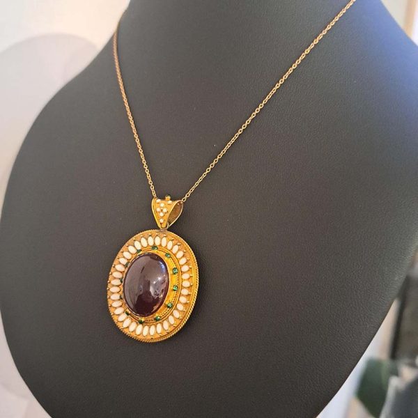 Antique Archaeological Revival Garnet Enamel and Gold Pendant, yellow gold pendant with large oval cabochon-cut garnet accented with white enamel and green enamel decorated surround