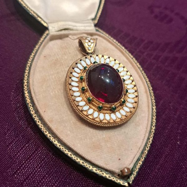 Antique Archaeological Revival Garnet Enamel and Gold Pendant, yellow gold pendant with large oval cabochon-cut garnet accented with white enamel and green enamel decorated surround