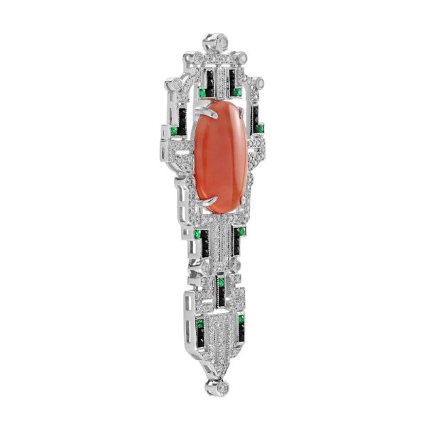 Art Deco Inspired Coral Onyx and Diamond Brooch, vivid orange 6.32ct oval coral within diamond geometric frame with contrasting black onyx and green emerald accents in 14ct white gold