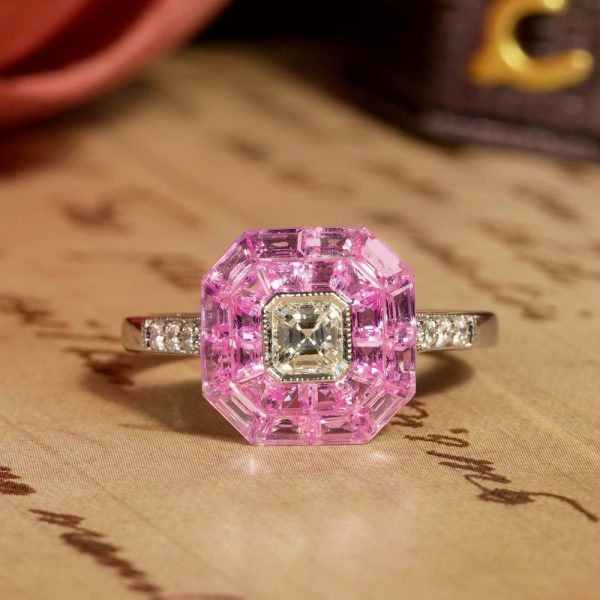 Asscher Cut Diamond and Pink Sapphire Engagement Ring, 0.30ct Asscher-cut diamond is surrounded by invisible set vibrant pink sapphires creating solid solitaire design in 18ct white gold with diamond-set shoulders
