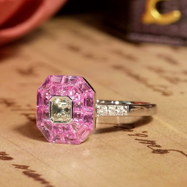 Asscher Cut Diamond and Pink Sapphire Engagement Ring, 0.30ct Asscher-cut diamond is surrounded by invisible set vibrant pink sapphires creating solid solitaire design in 18ct white gold with diamond-set shoulders