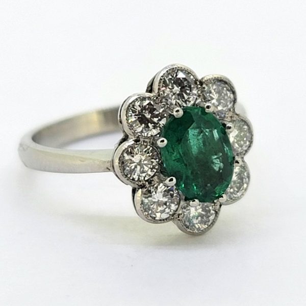 1.10ct Emerald and Diamond Floral Cluster Engagement Ring, 1.10ct oval emerald surrounded by 0.96cts round brilliant-cut diamonds in classic flower design in 18ct white gold