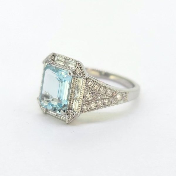 Contemporary Aquamarine and Diamond Cluster Dress Engagement Ring in 18ct White Gold, 1.85ct emerald-cut aquamarine surrounded by baguette-cut diamond halo with brilliant diamond accents to each corner with tapered diamond-set shoulders