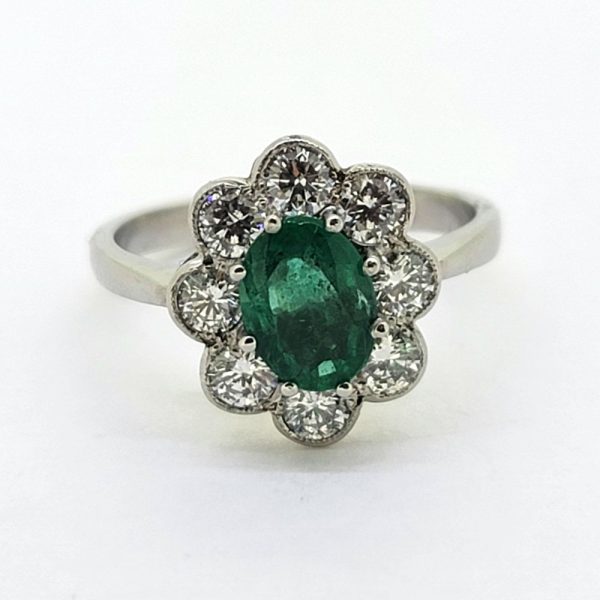 1.10ct Emerald and Diamond Floral Cluster Engagement Ring, 1.10ct oval emerald surrounded by 0.96cts round brilliant-cut diamonds in classic flower design in 18ct white gold